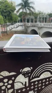 Libro turístico en parque con puente y palmera en fondo, lugar emblemático de Colombia.