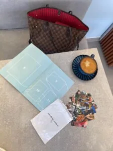 Alto texto: Bolsa de Louis Vuitton con interior rojo, junto a fotos, un libro y una taza de café en una mesa.
